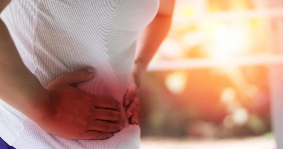Close-up of a woman clutching her lower right abdomen, with a red overlay indicating pain from Crohn’s Disease in Modesto, CA.