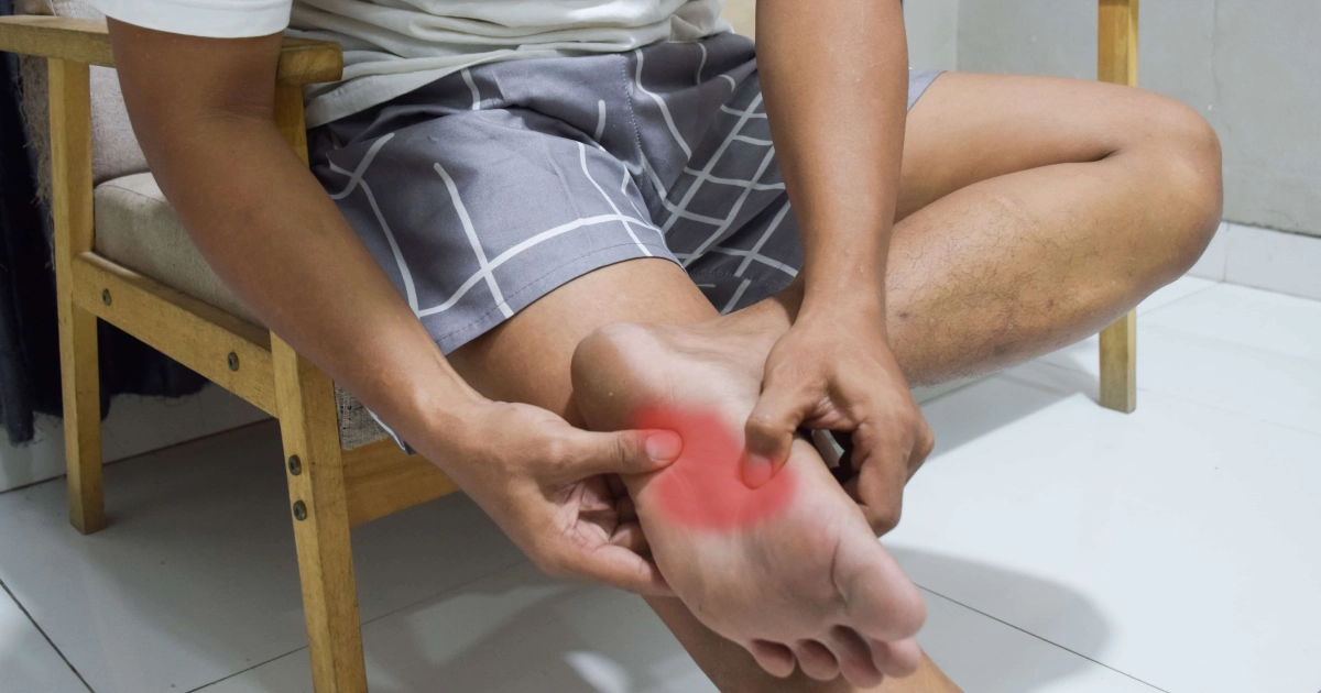 Young man showing pain in leg from gout in Modesto, CA, holding his foot and grimacing due to discomfort.